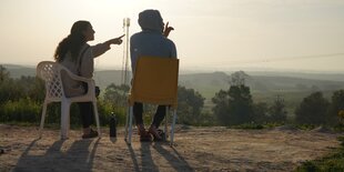 Menschen sitzen auf Stühlen im Freien und deuten in die Ferne