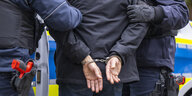 Polizisten führen eine Person in Handschellen ab.