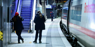 Bahnsteig im Hamburger Hauptbahnhof mit eingefahrenem Zug. drei Personen stehen am Gleis. Mindestens eine davon ist Bahnmitarbeiterin, erkennbar an der Uniform und der roten Mütze.