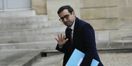 Frankreichs Außenminister Séjourné geht an einer Hauswand vorbei, schaut dabei seitlich in die Kamera und winkt