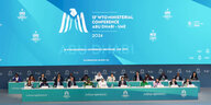 Ein Foto der WTO-Konferenz in Abu-Dhabi. Man sieht Menschen auf einem Podium sitzen.