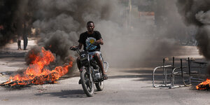 Ein Rollerfahrer fährt an einer brenndenen Barrikade vorbei