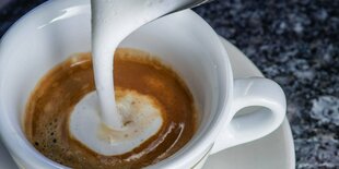 In eine Tasse Cappuchino wird Milchschaum gegossen