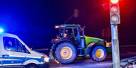 Nachts: Polizei mit Blaulicht im Vordergrund und eine Ampel steht auf Rot, dahinter ein Traktor