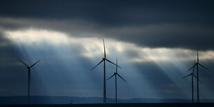 Die Sonne bricht hinter Windrädern durch die Wolkendecke.