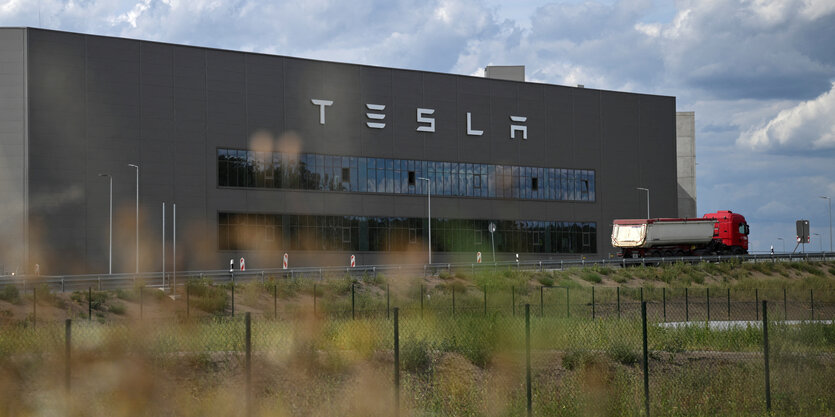 Blick auf die Gigafactory in Grünheide, im Vordergrund eine Straße und Zäune