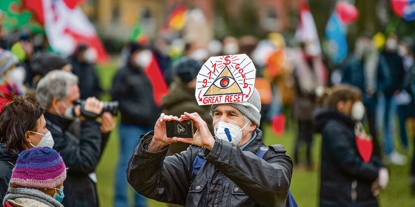 Ein Teilnehmer einer Demonstration gegen die Corona-Politik trägt eine Kopfbedeckung mit der Aufschrift "911 - $ - Covid - Great Reset".