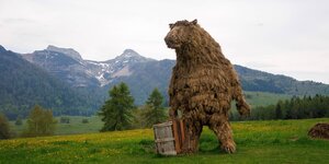 Strohskulptur eines Bären vor Alpenkulisse