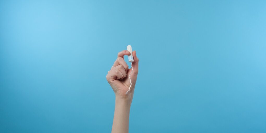 Eine Hand vor blauem Hintergrund hät einen Tampon