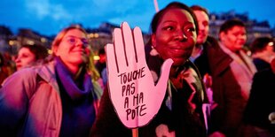 Eine Frau hält eine Hand aus Pappe auf der die französischen Worte "Touche pas ma pote" zu lesen sind