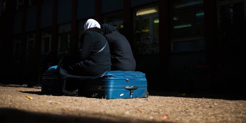 Zwei Frauen mit Kopftüchern sitzen auf einem großen, blauen Koffer