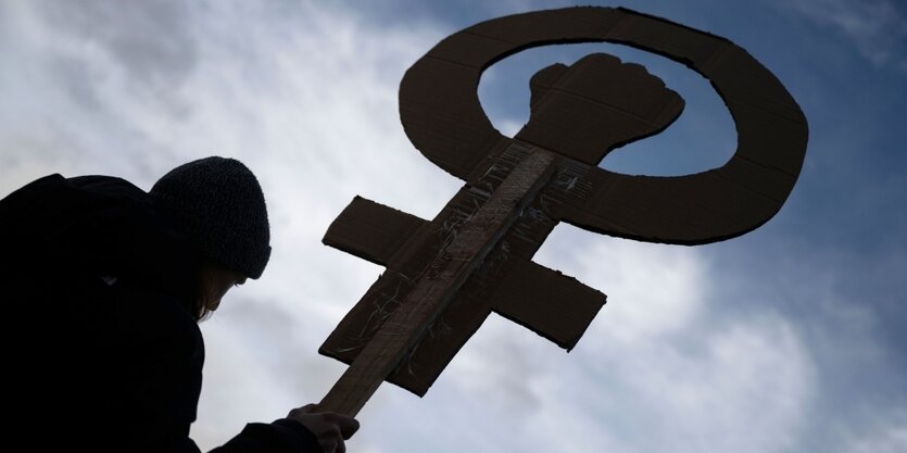 Silhouette einer Frau, die ein Frauenzeichen aus pappe in der hand hält