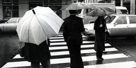 PassantInnen mit Regenschirmen überqueren im Jahr 1980 eine Straße in Paris.