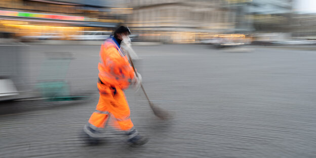 Ein Mann in orangener Arbeitskleidung fegt die Straße.