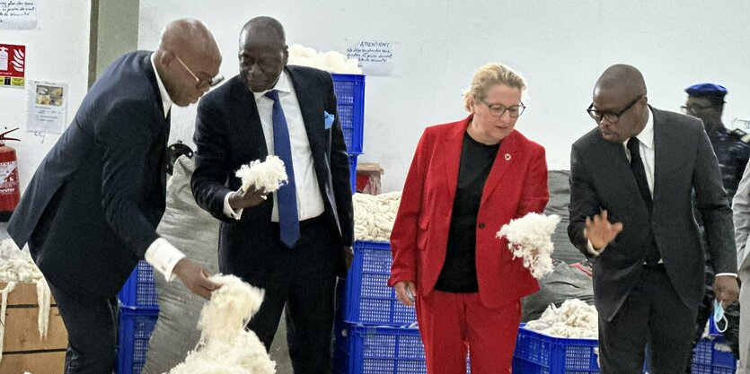 Svenja Schulze im roten Anzug und mehrere Männer besichtigen Baumwollfabrik.