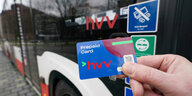 Eine Hand hält eine HVV-Prepaid-Karte in die Kamera, dahinter ist ein Bus zu sehen