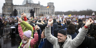 Eine Menschenmenge steht vor dem Bundestag. Sie heben die Arme, halten sich teilweise gegenseitig an den Händen. Im Hintergrund die Kuppel des Reichstagsgebäudes.