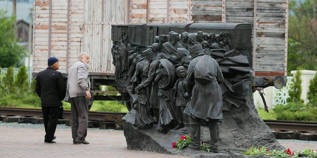 Menschen stehen an einem Denkmal, dass Menschen vor einem Waggon zeigt