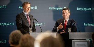 Lindner steht links, Heil rechts auf einem Podium. Heil spricht in ein Mikro und gestikulirert. Lindner steht steif rum. Vor ihnen Menschenköpfe.