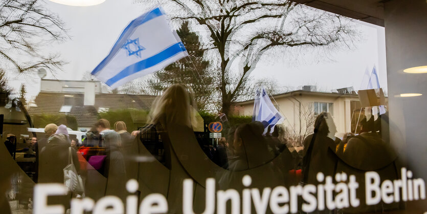 Eine Israel-Flagge spiegelt sich bei einem stillen Protest einer Initiative für die Sicherheit jüdischer Studierender in einer Scheibe der Freien Universität Berlin.