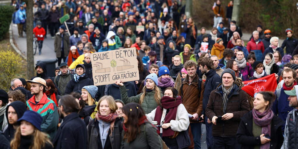 Protestmarsch in Grünheide - auf einem Schild wird gefordert: Bäume statt Beton - Stoppt Giga Factory