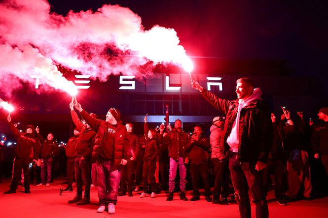 Junge Männer stehen mit Fackeln in der Hand, die roten Rauch erzeugen, vor der Tesla GigaFactory, um gegen den Brandanschlag auf einen Strommasten zu protestieren