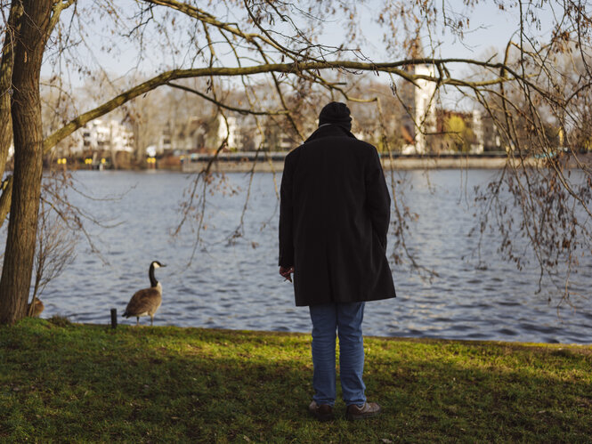 Oliver Vorthmann von hinten am Ufer eines Gewässers, er blickt auf einen Vogel