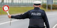 Ein Bundespolizist auf dessen Jacke das Wort Polizei steht an einer Straße und hält eine rote Kelle raus: Halt Polizei
