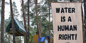 Ein Transparent mit der Aufschrift "Wwater is a human richt" hängt zwischen den Bäumen im Camp von Aktivisten der Initiative "Tesla stoppen" nahe der Tesla-Gigafactory Berlin-Brandenburg.