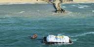 Luftaufnahme: Man sieht einen Lastkahn, der vor einem provisorischen Landungssteg liegt, daneben befindet sich ein Schlauchboot
