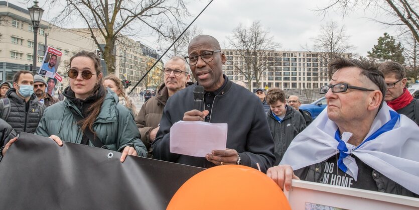 Menschen mit Transparenten auf der Straße, ein Mann in der Mitte mit Mikrofon in der Hand