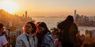 Menschen stehen auf einem Aussichtsberg und schauen auf die Kulisse von Hongkong