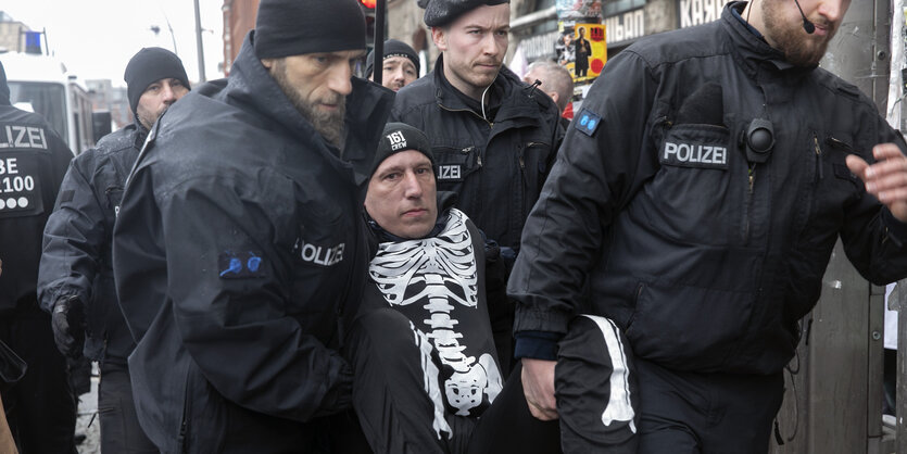 Ein Mann wird von mehreren Polizisten weggetragen