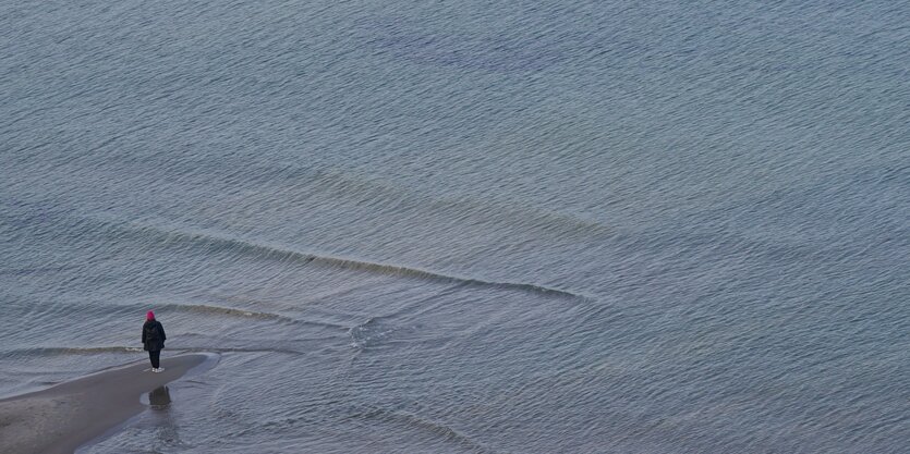 Eine Person steht auf einer kleinen Landzunge an der Ostsee