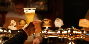 Ein Mensch umschließt ein Bierglas und zeigt mit dem Finger