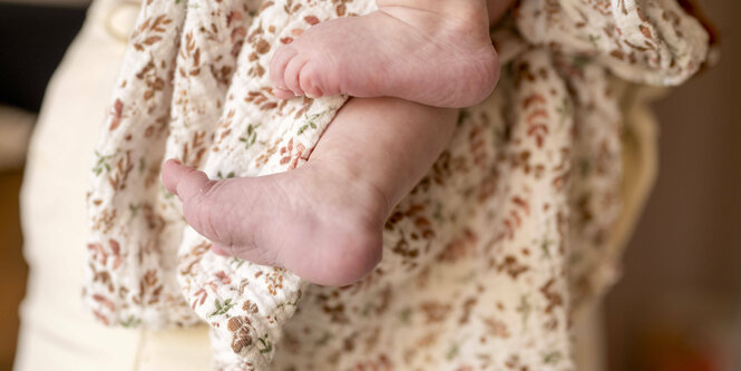 Eine Frau hält ein kleines Baby auf dem Arm, wir sehen nur die kleinen füsse in Hüfthöhe