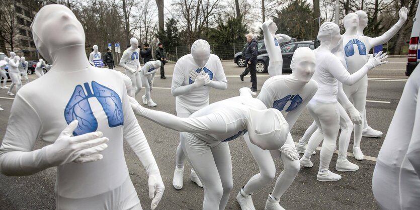 Weiß eingehüllte Figuren mit blauen Lungen im Oberkörperbereich bei einer aktion auf der Strasse