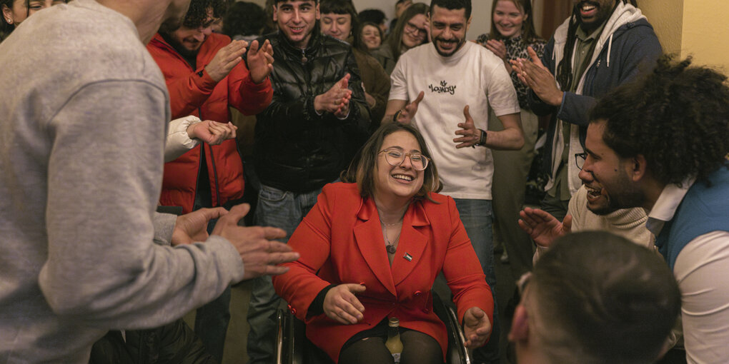 Fatima im Rollstuhl steht in der Mitte einer Partygesellschaft, alle klatschen und lachen