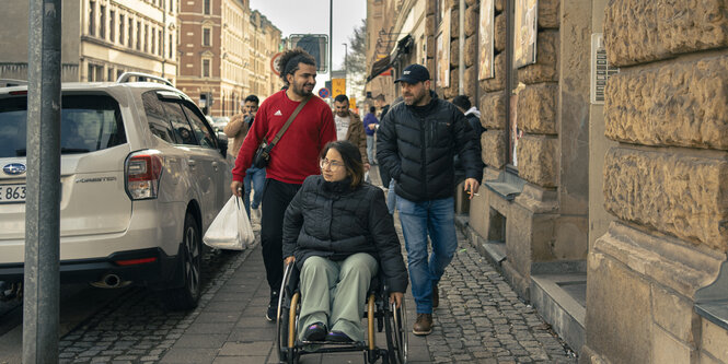 Fatima Maged fährt fröhlich im Rollstuhl mit Unterstützern durch Chemnitzer Straßen