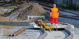 Eine Person mit Warnweste steht mit Arbeitsgeräten auf Schienen, die vor einem Schutthaufen enden