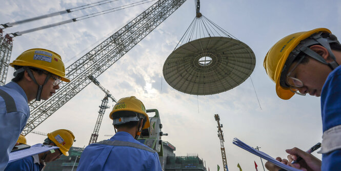 Chinesen mit gelben Bauhelmen, ein Betondekcel an einem Kran