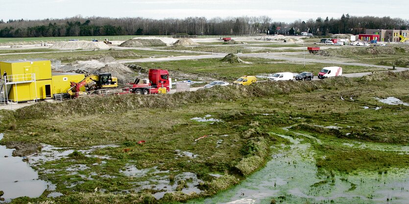 Ein Gelände mit Erdhügeln und Grasflächen. Dazwischen stehen Fahrzeuge und Büro-Container.