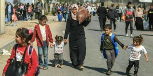 Frauen und Kinder mit Koffern laufen entlang einer Straße