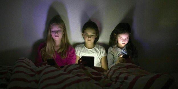 Drei Mädchen spielen mit ihren Smartphones im Bett