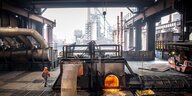 Blick ins Bremer Stahlwerk, ein Arbeiter läuft an einem glühenden Schmelzofen vorbei