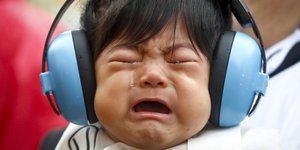 Kind mit Ohrenschützern verzieht Gesicht, wahrscheinlich vor Lärm