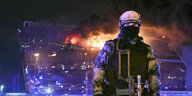 Ein vermummter und bewaffneter Soldat steht vor der brennenden Konzerthalle in der Nacht