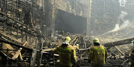 Zwei Männer in Feuerwehruniformen stehen in der Ruine der Crocus City Hall