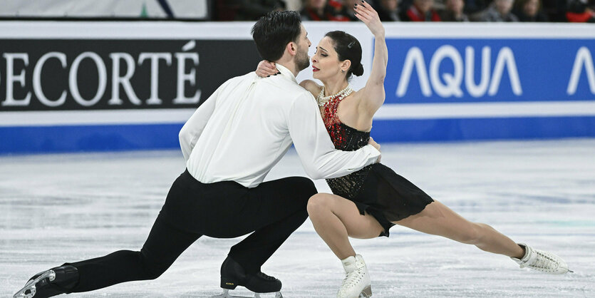 Deanna Stellato-Dudek mit ihrem Partner Maxime Deschamps bei ihrer Kür auf dem Eis. Beide haben ein Bein weit nach hinten gestreckt, mit dem anderen gehen sie in die Hocke. Sie umarmen sich und befinden sich Nase an Nase.