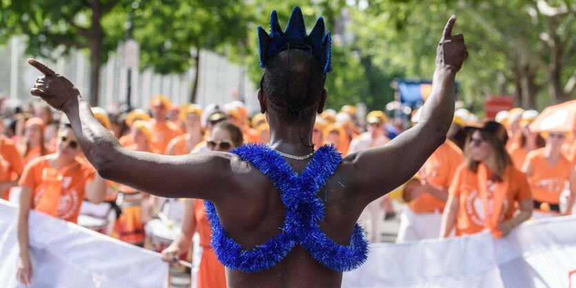 Ein Teilnehmer im Neptun Kostüm von Hinten und im Hintergrund Musiker beim Karneval der Kulturen